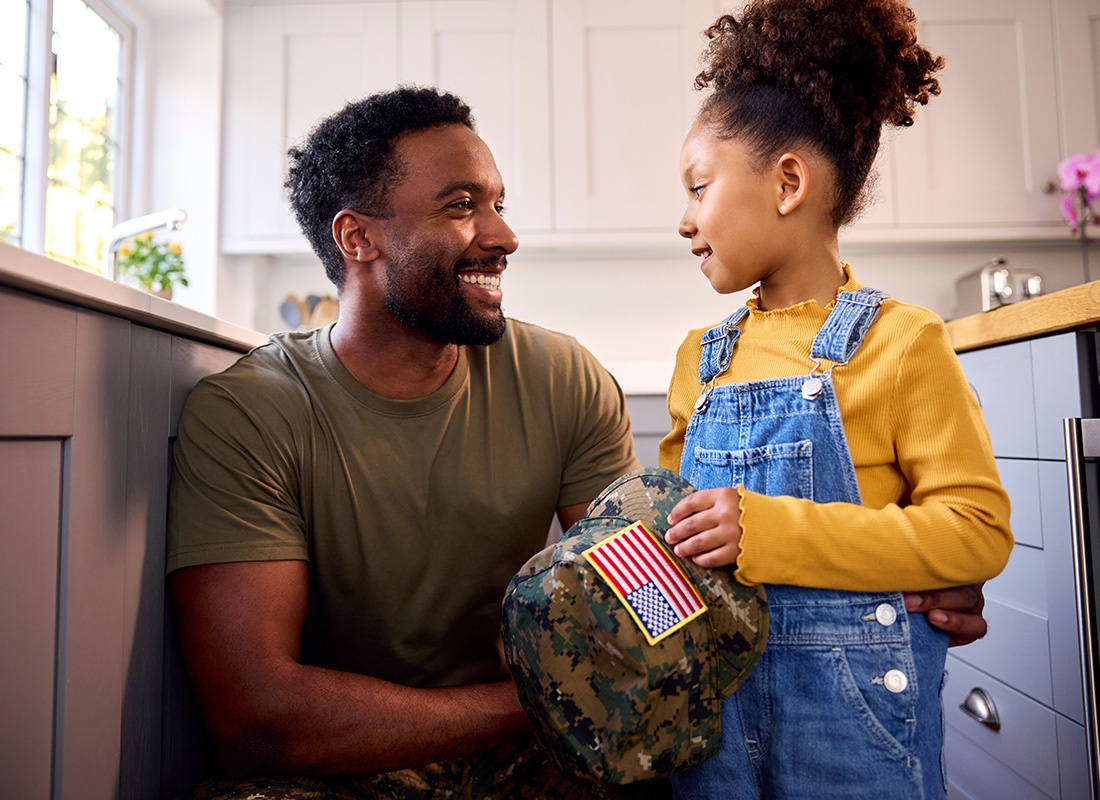 About Our Agency - Smiling Portrait of a Father Wearing an Army Uniform Standing Next to his Daughter in the Kitchen Holding an Army Cap