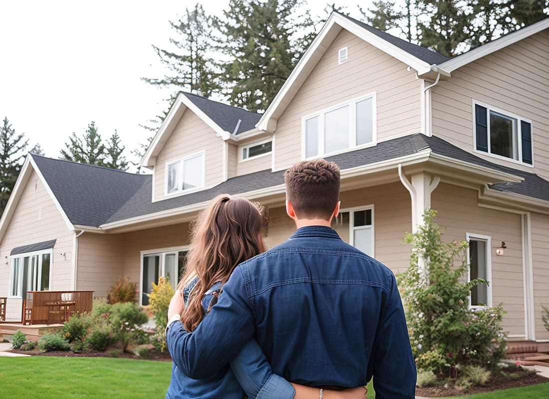Personal Insurance - Rear View of a Young Married Couple Standing Outside Their New Two Story Home
